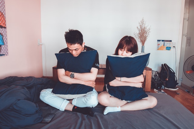 Muž a žena sedia vedľa seba na posteli a objímajú modré vankúše