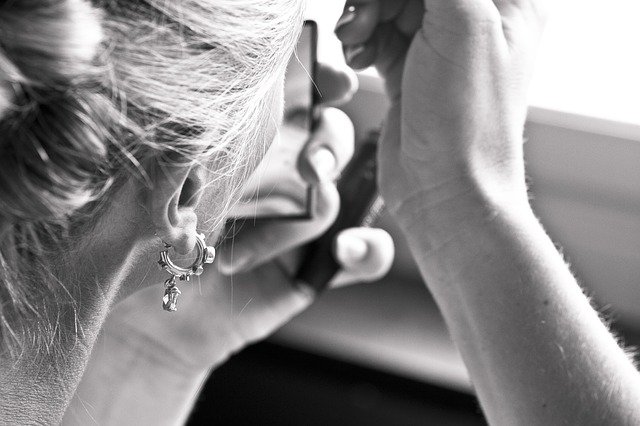 Detail na ucho ženy s náušnicou, ktorá sa maľuje pri malom zrkadielku.jpg